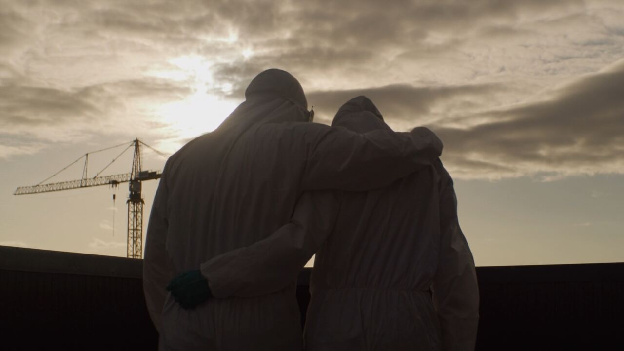 Two people in protective suits looking out over a city