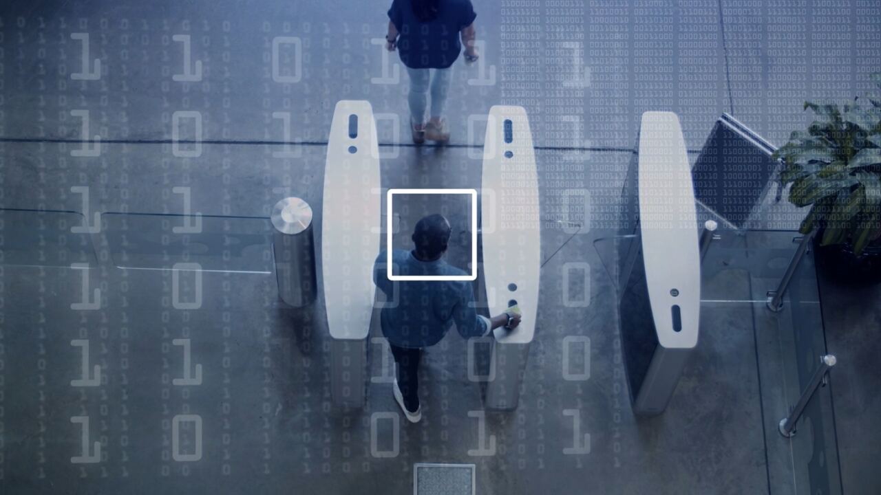 People passing through security gates over a pattern of binary code