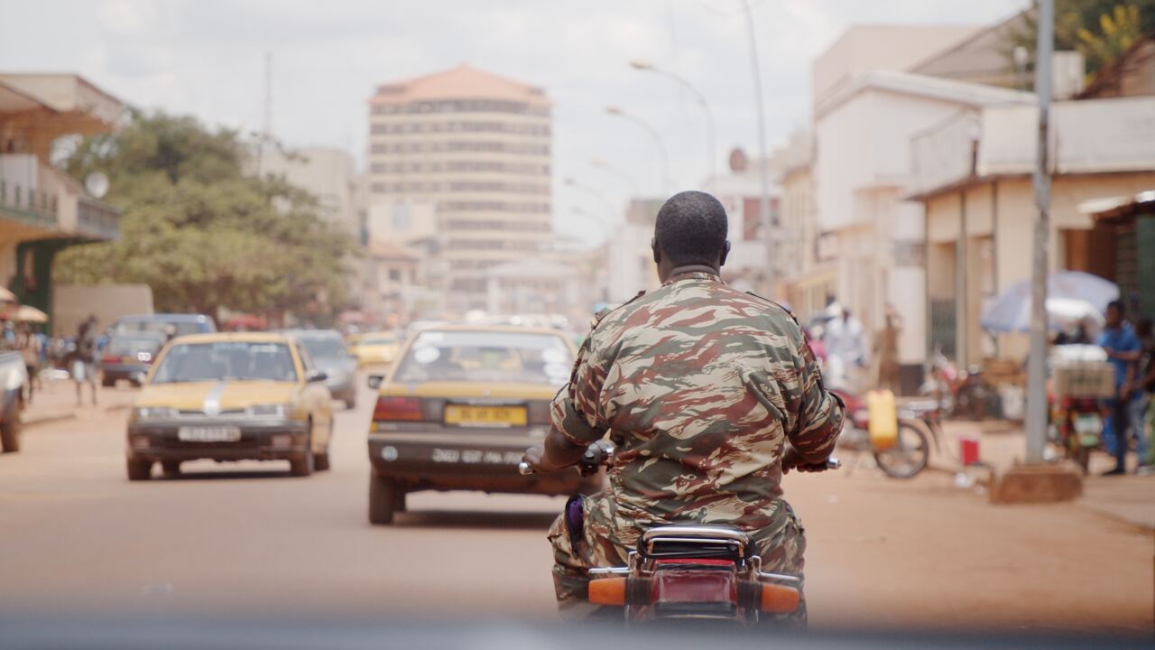 A soldier riding a motorbike through city traffic