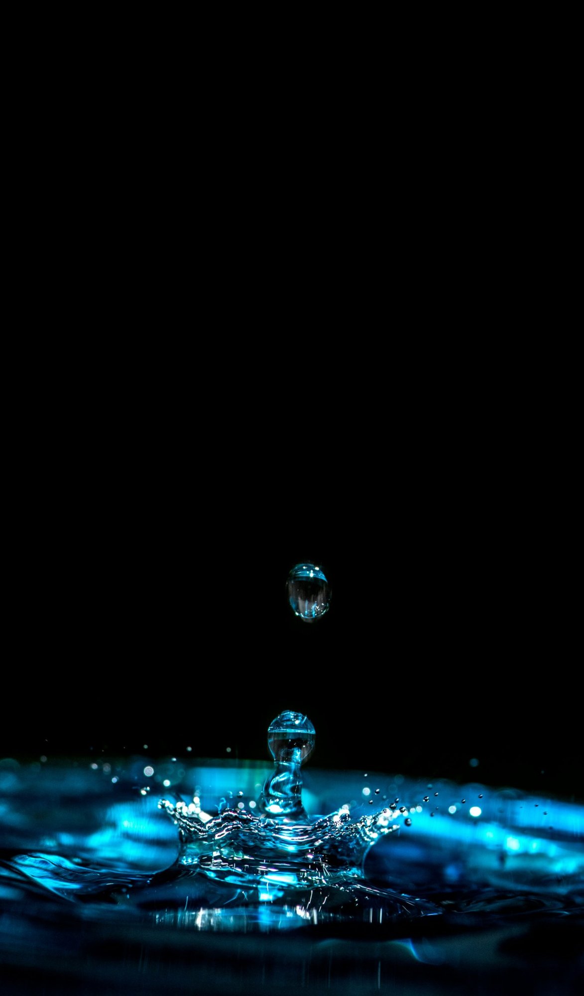 A water drop splashing into blue water against black