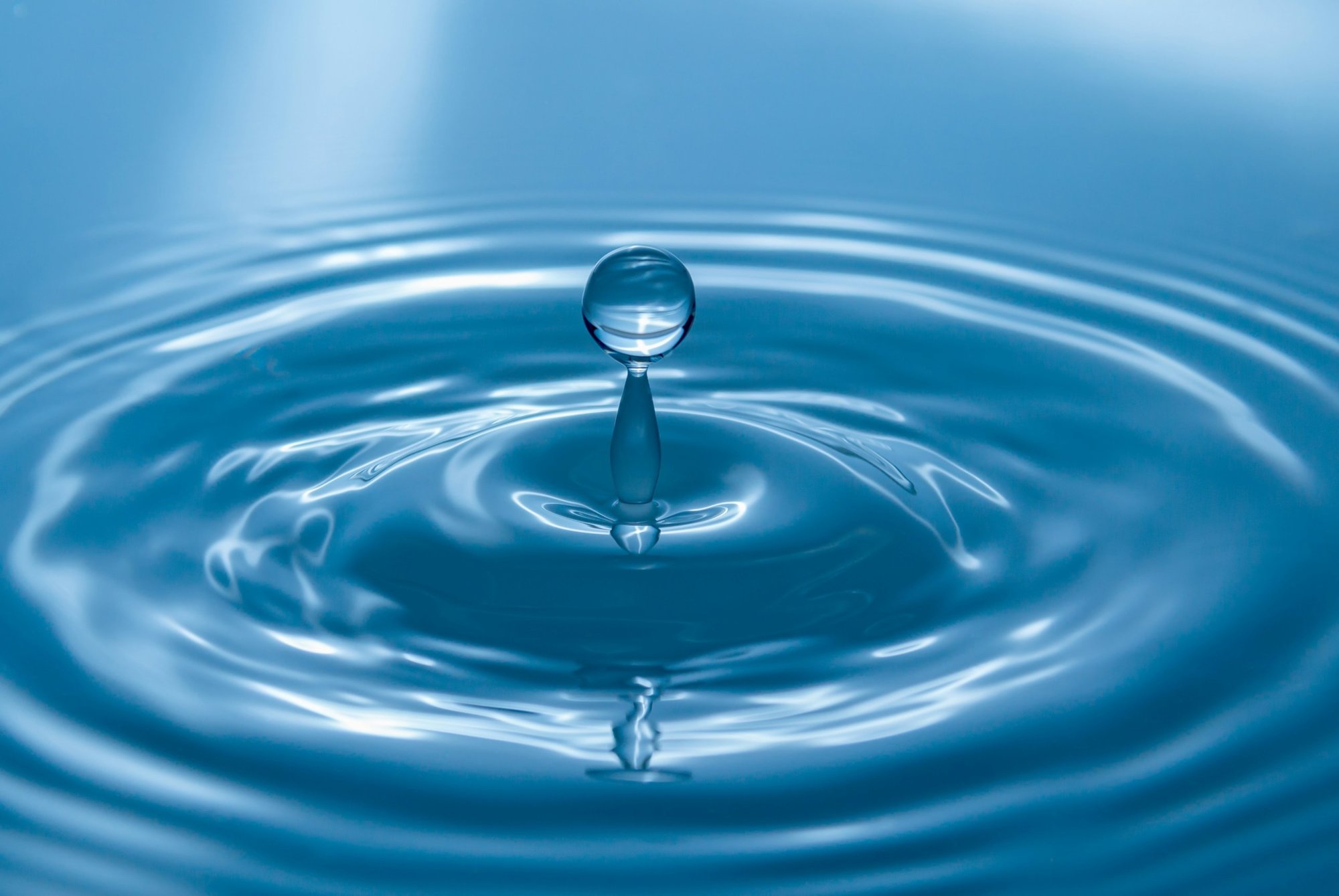A drop of water falling into still blue water, sending out ripples