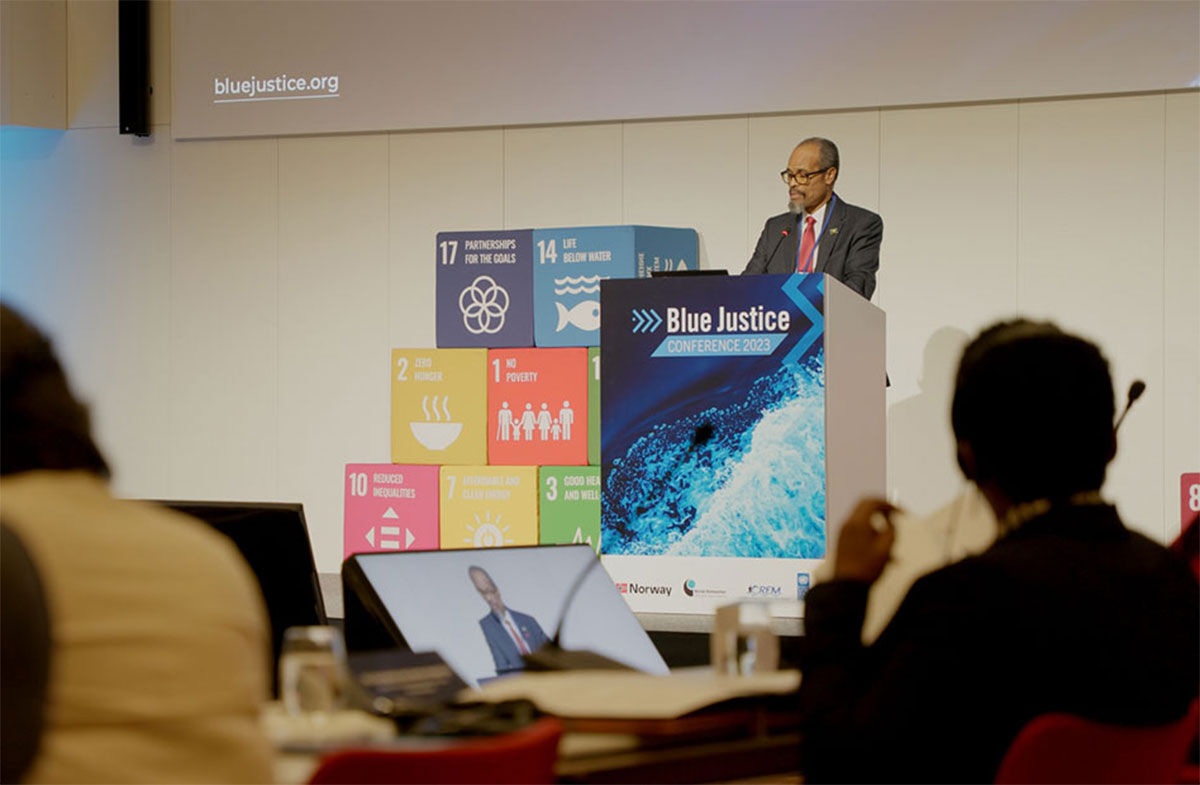 A minister speaking at a Blue Justice lectern in front of the Sustainable Development Goals