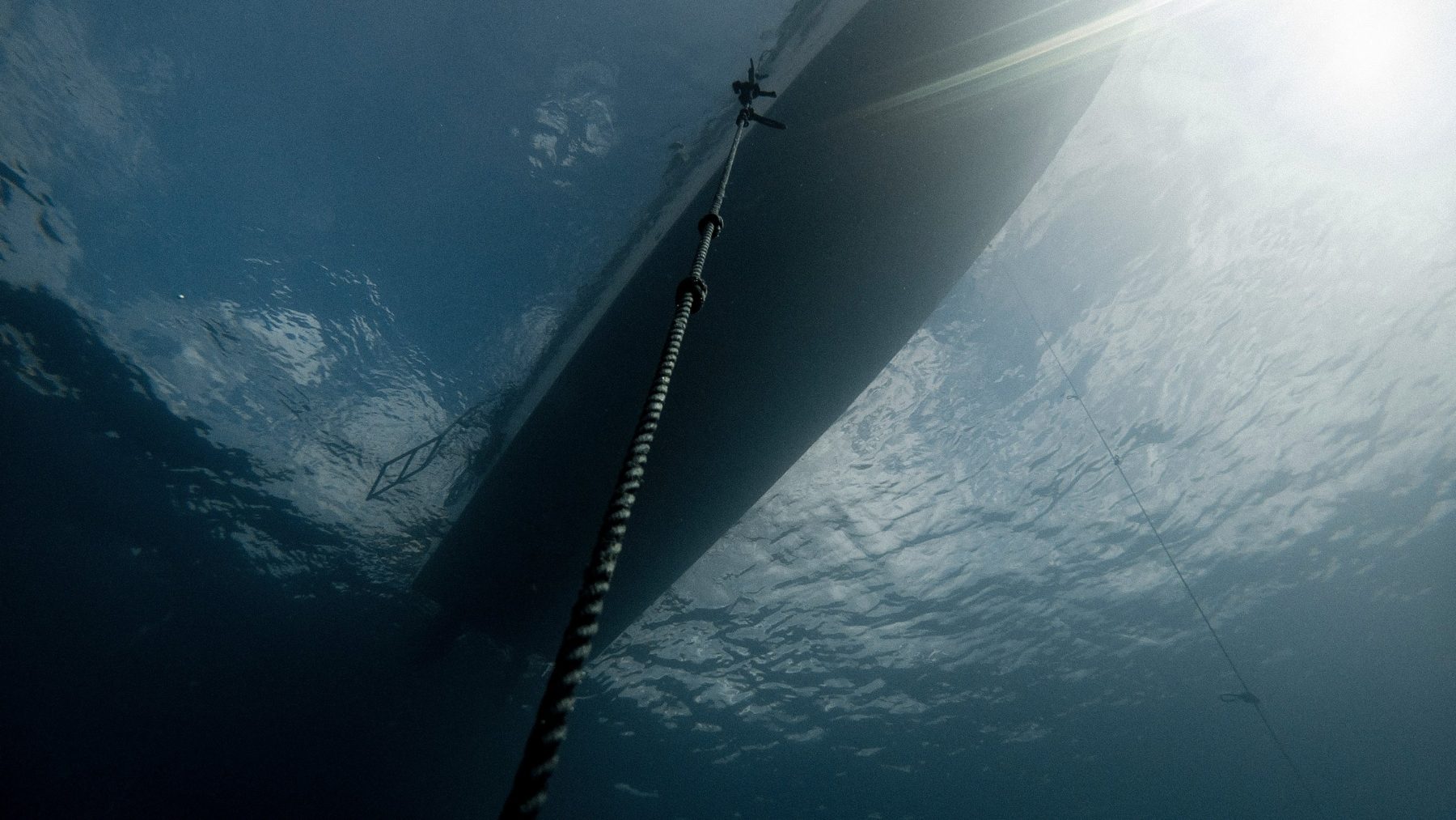 A mooring line rising to a boat hull, seen from underwater