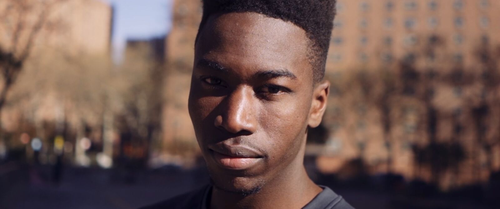 Film still: a young man looking into the camera on a city street