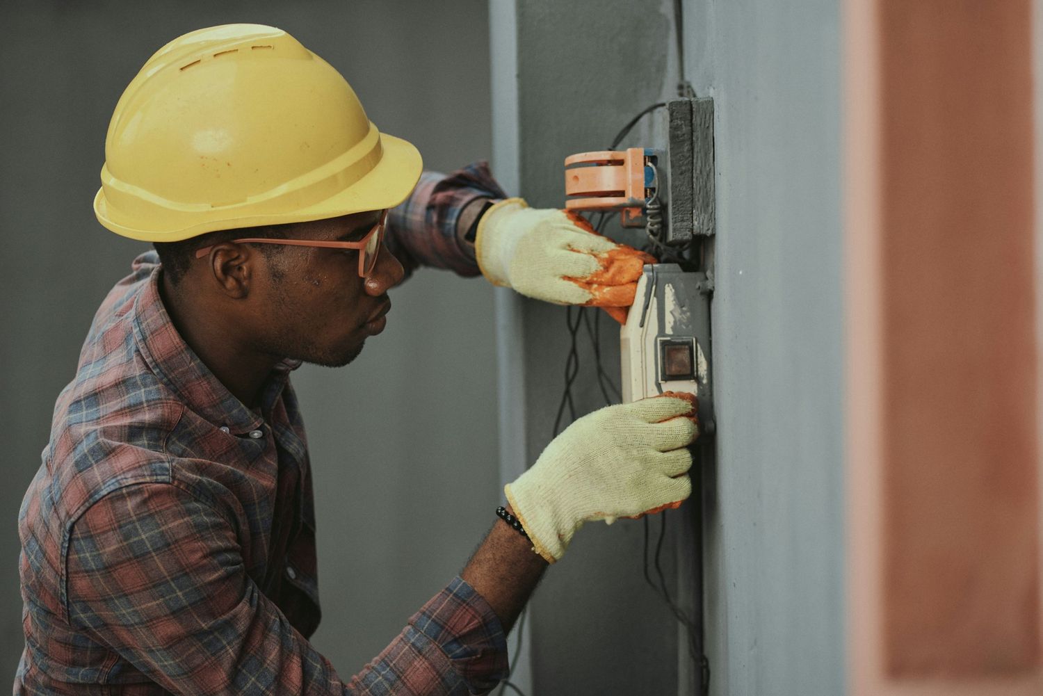An electrician in a hard hat working on a wall-mounted switch box