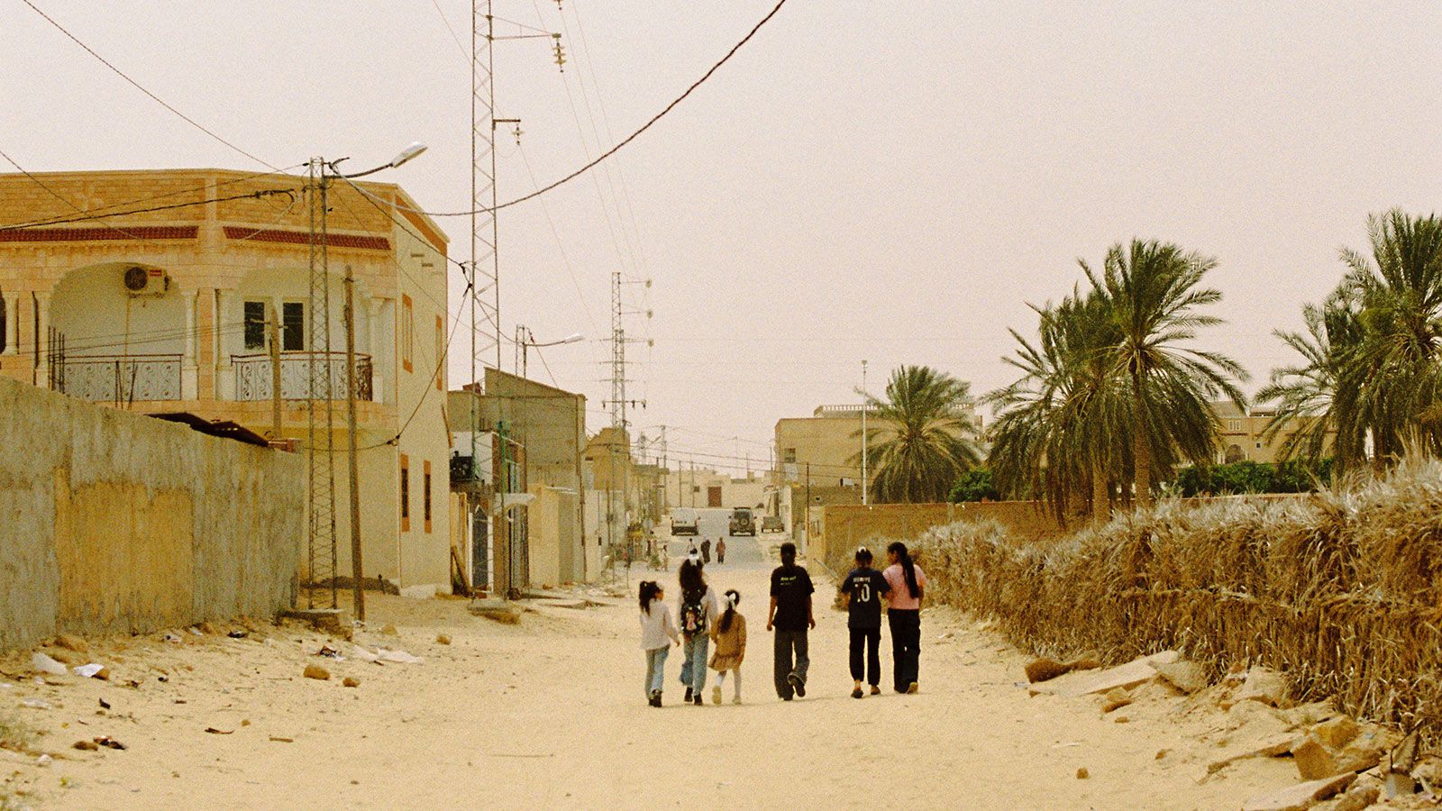 Children walking down a sandy street lined with power lines