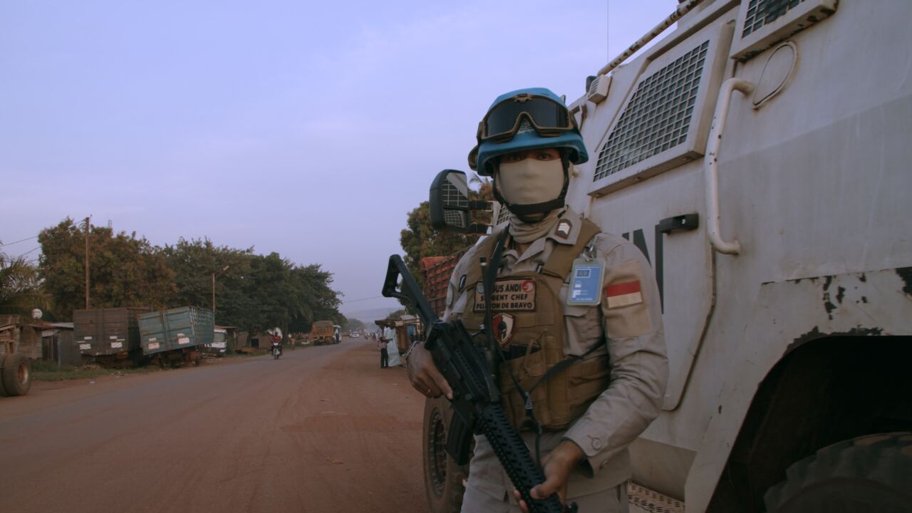 A UN peacekeeper standing guard beside an armoured vehicle