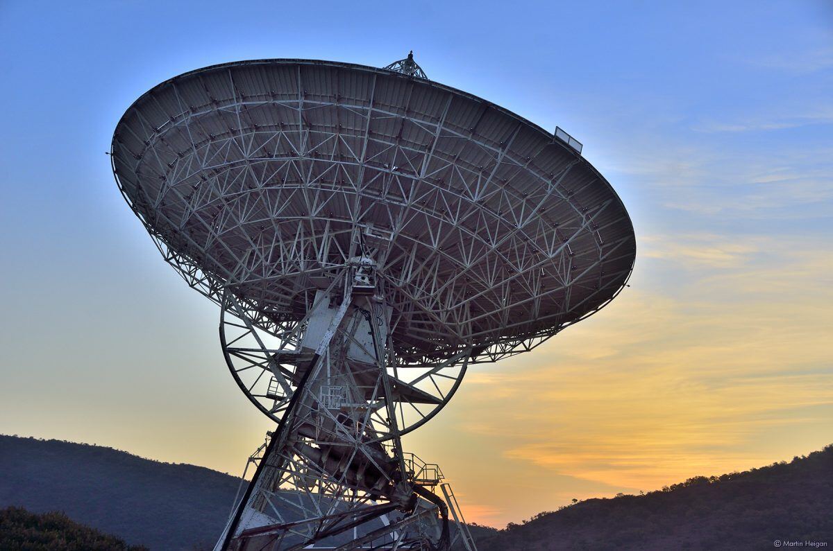 A radio telescope dish against a sunset sky