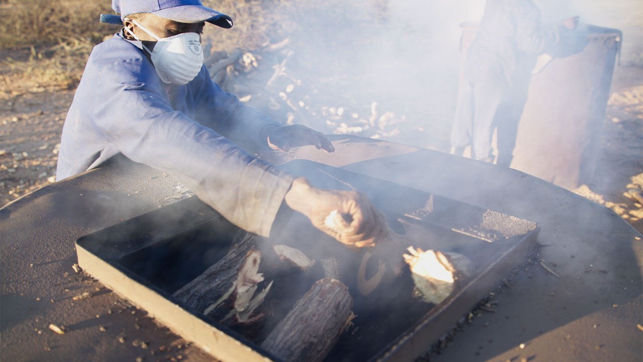 A worker in a dust mask tending a charcoal kiln