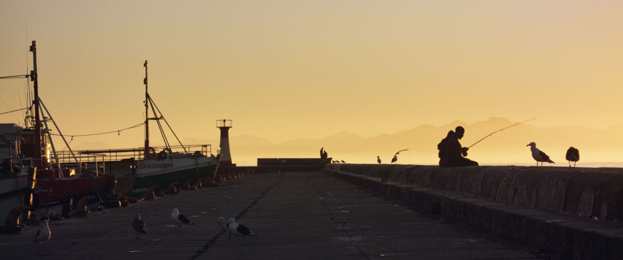 A fisherman on a harbour wall at sunset