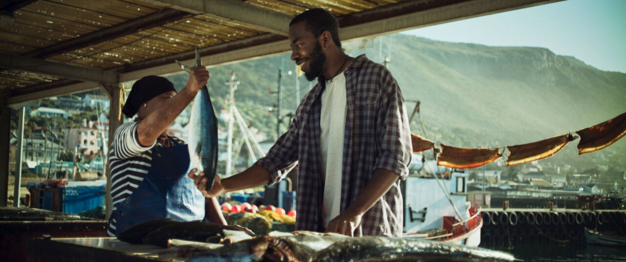 A man buying a whole fish from a fisherwoman at the harbour