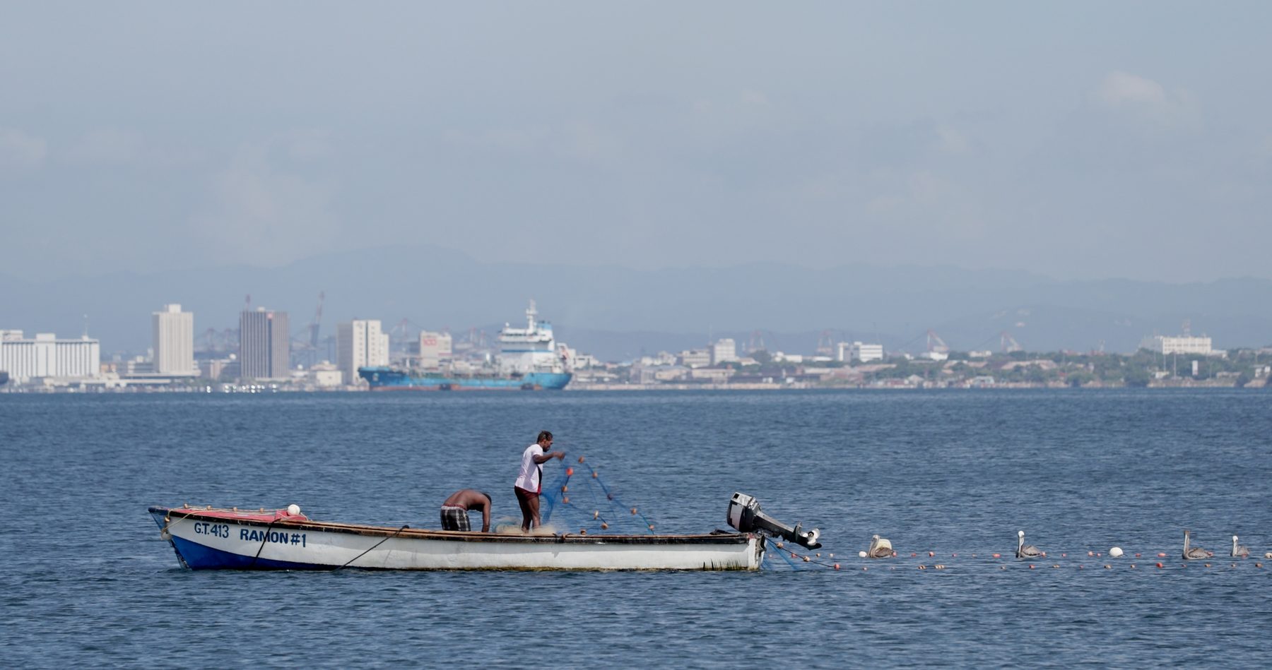 Two fishers hauling a net from an open boat in Kingston harbour, Jamaica